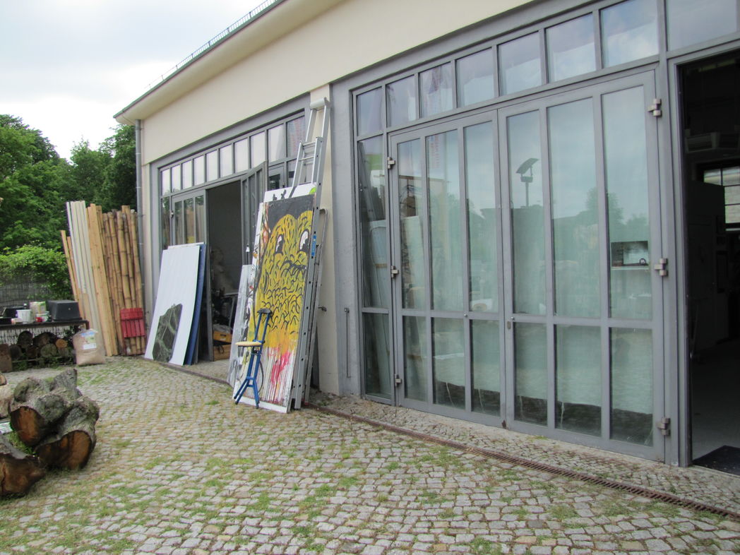 Eingangsbereich mit lichtoffenen Fenstern und angelehnten Gem&auml;lden am K&uuml;nstleratelier